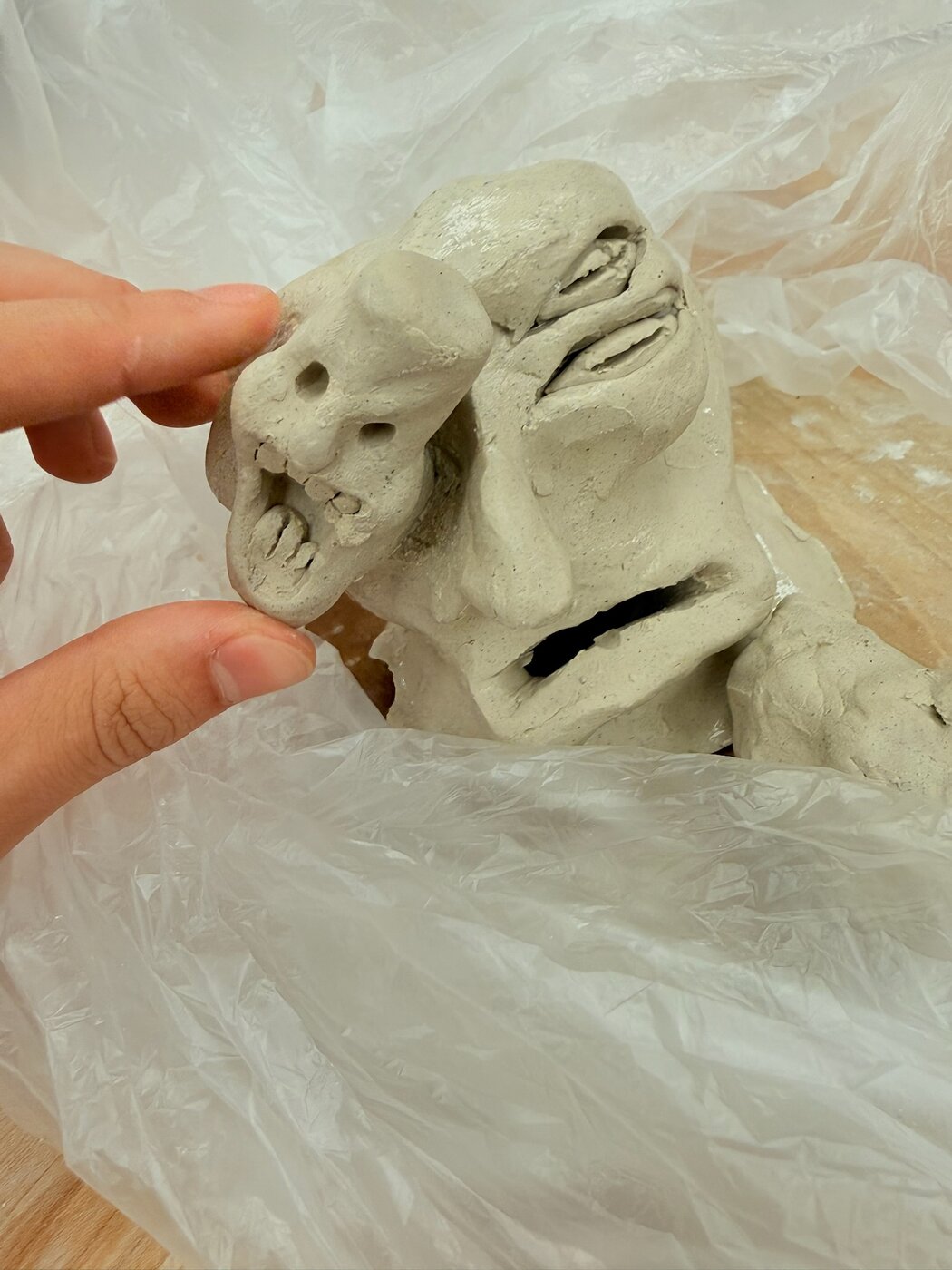 Hand-built two-faced clay sculpture with expressive features, shown unfired